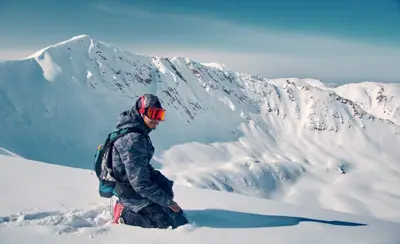 Backcountry skier kneeling on a snowy Himalayan ridge