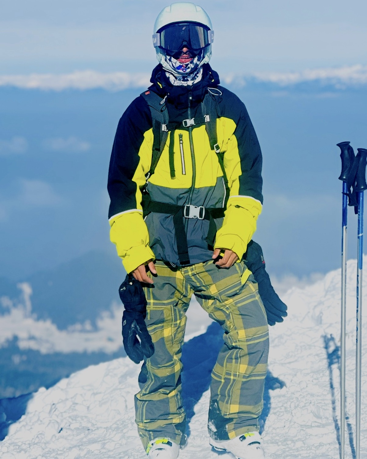 Aamir, ski guide, in a white helmet and yellow jacket on a snowy ridge